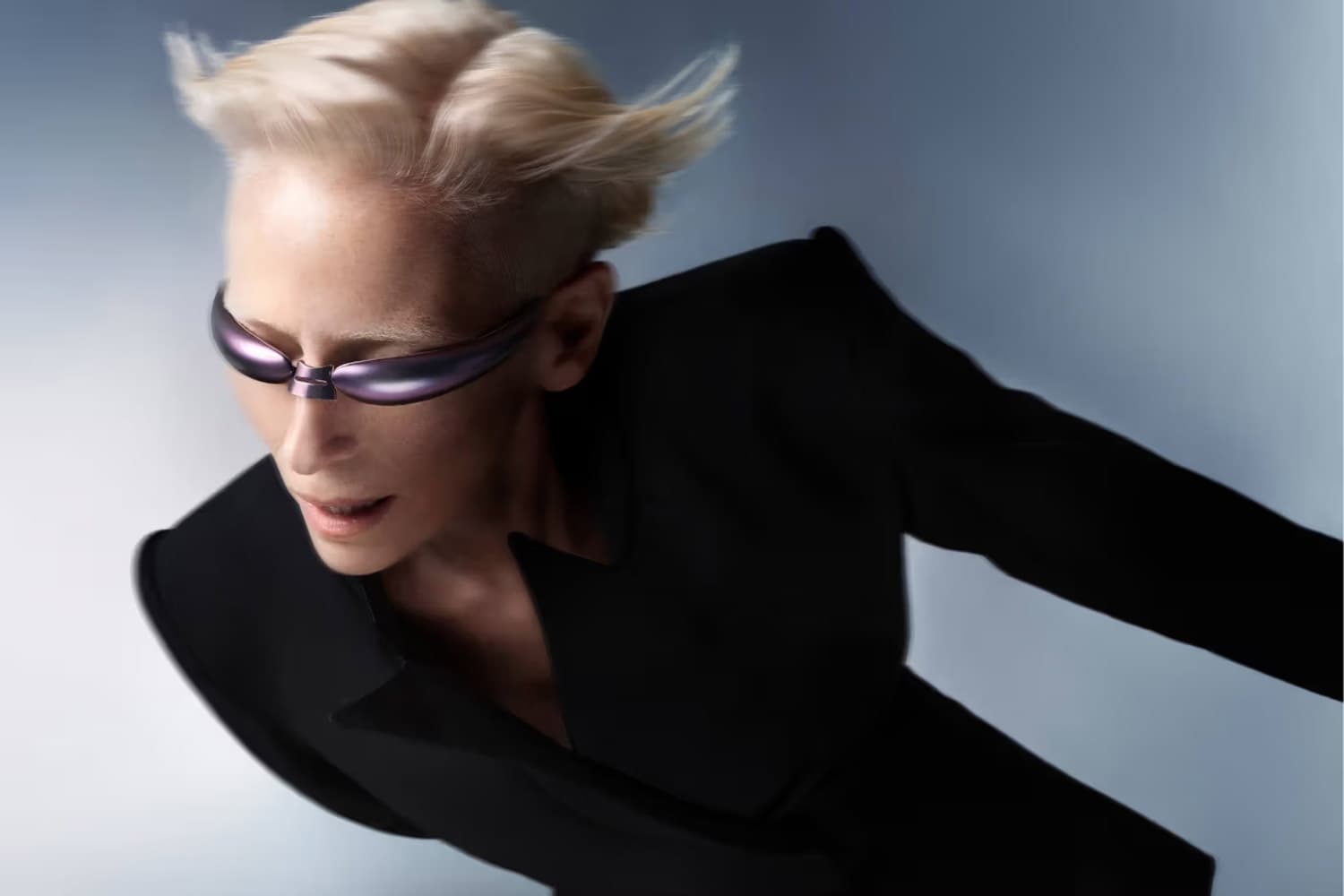 Tilda Swinton for Gentle Monster with short platinum hair wearing slim, futuristic sunglasses from the brand's BOLD collectionand a structured black outfit, captured in a dynamic pose against a soft gradient background.