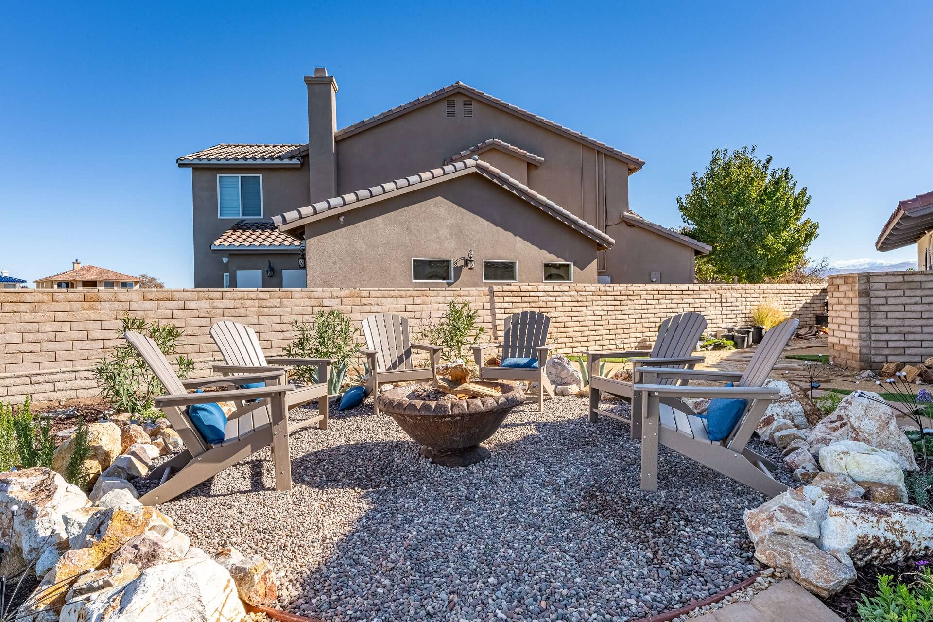 Backyard fire pit surrounded by outdoor chairs with blue rectangular pillows.