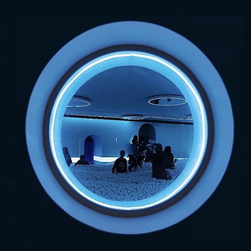 Persone che giocano in una vasca con palline viste attraverso una finestra circolare con illuminazione blu.