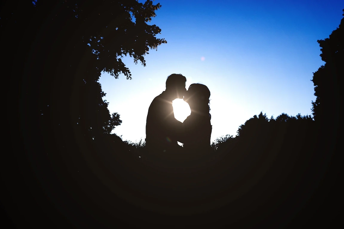 Bride and groom silhouetted at sunset sharing a kiss during their wedding