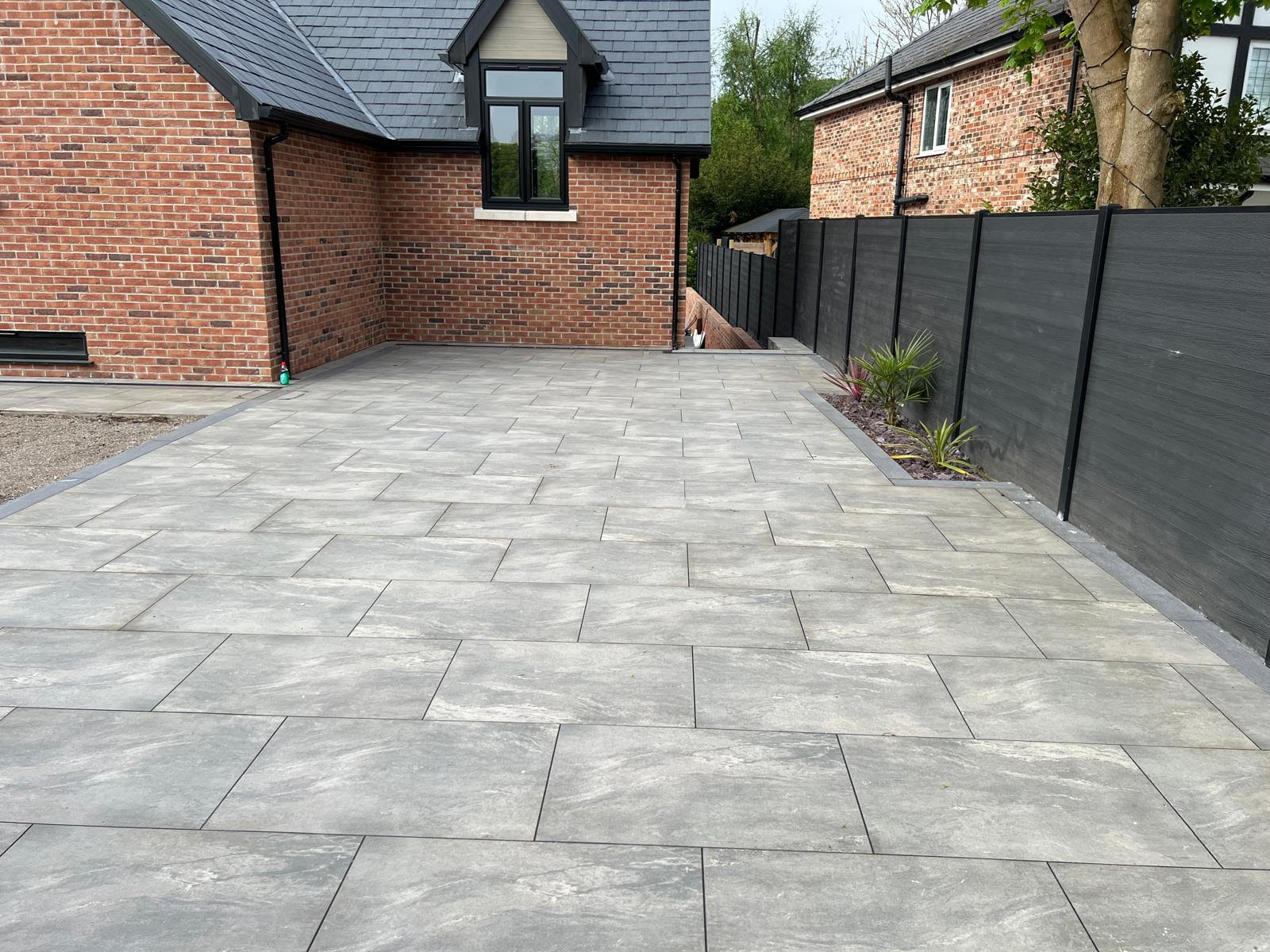 Luxury Alderley Edge Garden Transformation by LK Landscaping and Groundworks - Large-format grey slate patio tiles, modern dark fencing, and lush greenery create a sophisticated outdoor living space. Expert hardscaping and landscaping services for high-end residential properties in Alderley Edge, Cheshire.