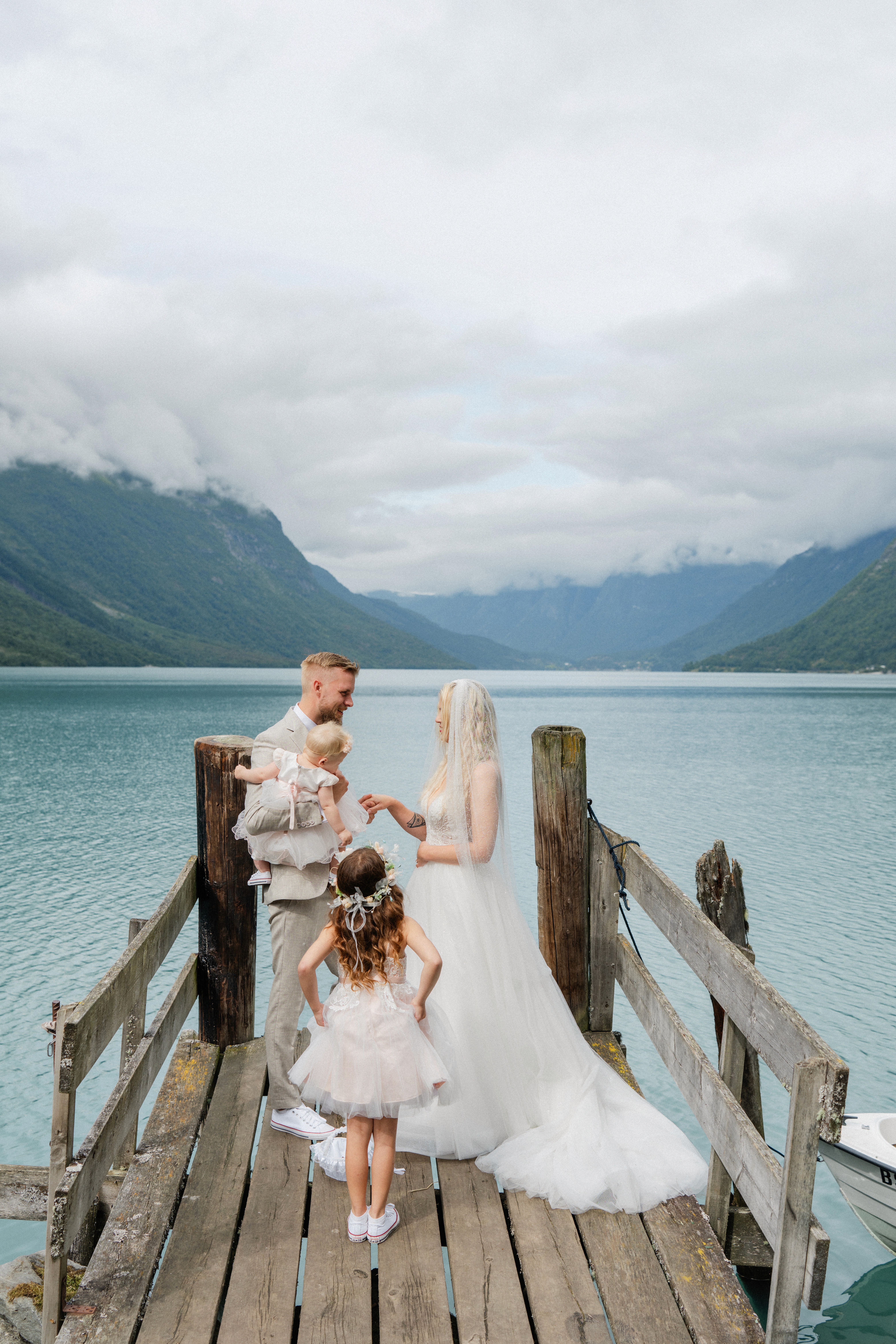 Wide view of the wedding couple and two children on a wooden jetty beside Lovatnet.