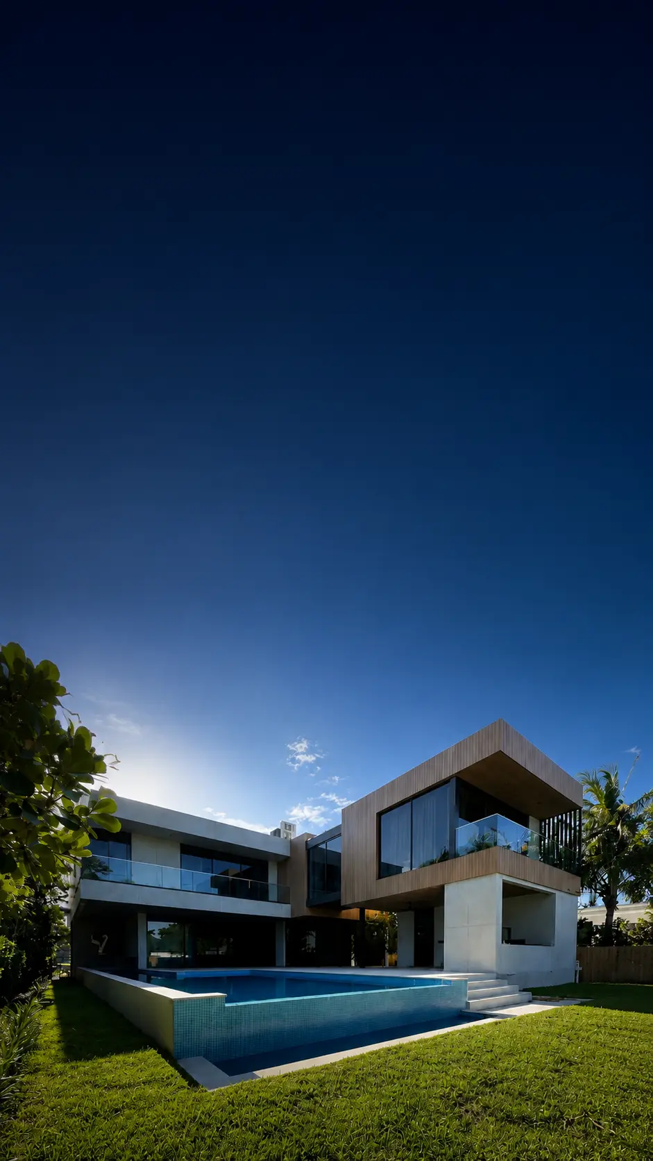 Modern two-story residential home in Miami Beach with floor-to-ceiling glass, wood-clad upper level, and a pool at dusk