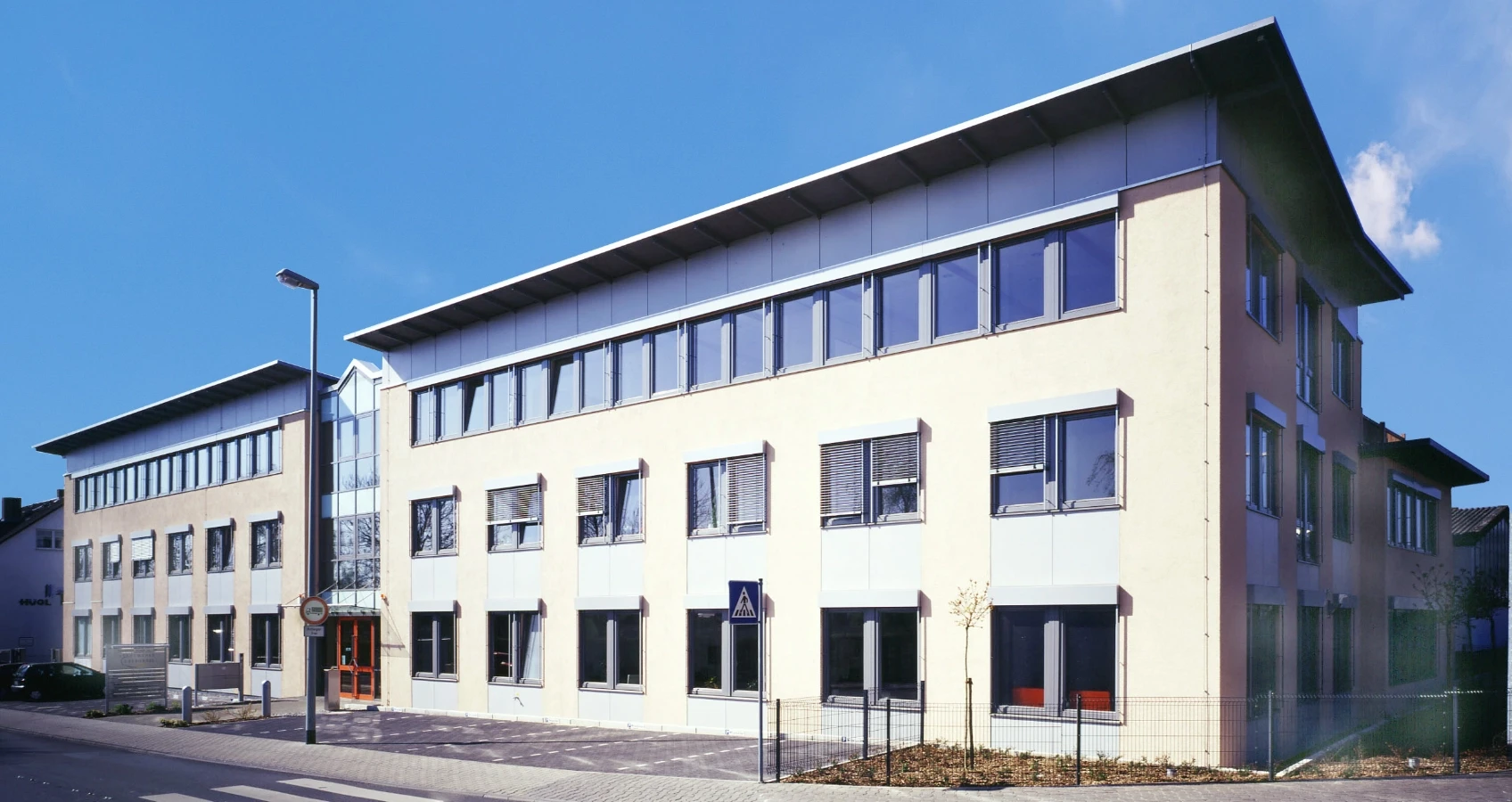 Modernes Bürogebäude mit heller Fassade und vielen Fenstern unter klarem blauen Himmel.