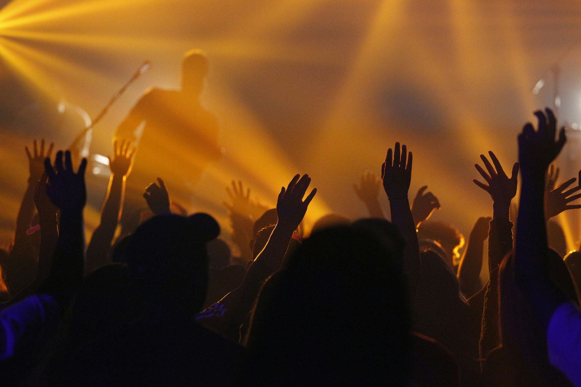Vor einer Bühne feiern Menschen mit erhobenen Händen. Gelbes Bühnenlicht erzeugt eine warme, fröhliche Stimmung und vermittelt einen positiven Festival-Vibe