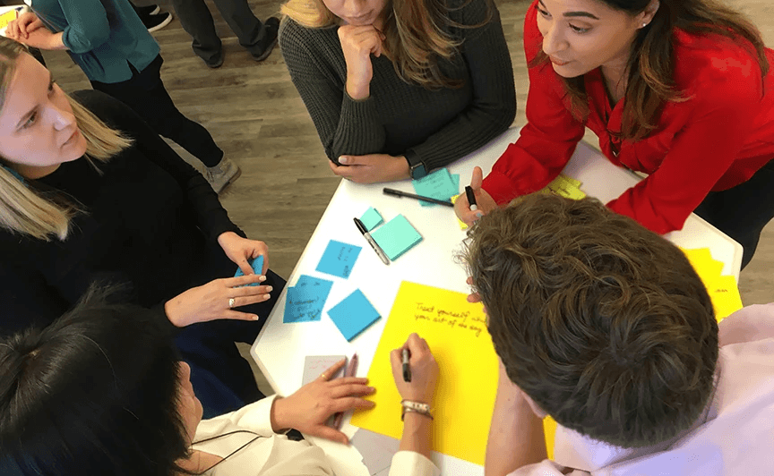Executives collaborate with sticky notes on a glass wall during a change management workshop to streamline workflows for new operational model