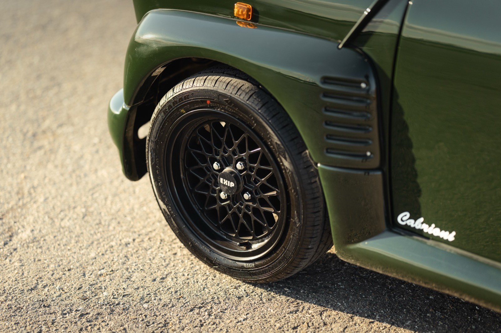 Close-up of a black alloy wheel on a green vehicle, showcasing the wheel arch and tire tread.