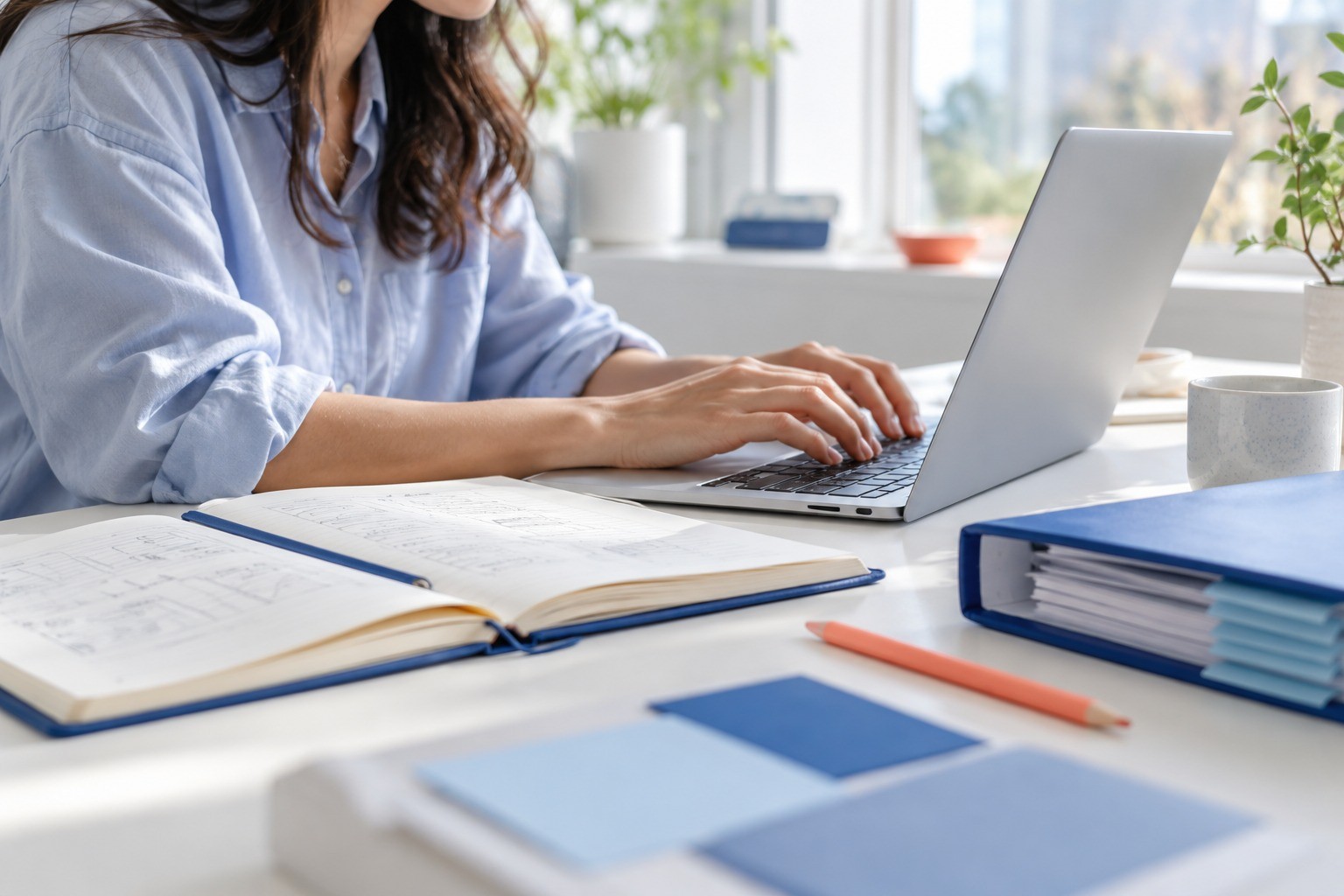 A developer’s hands working beside an open reference notebook and blue binder.