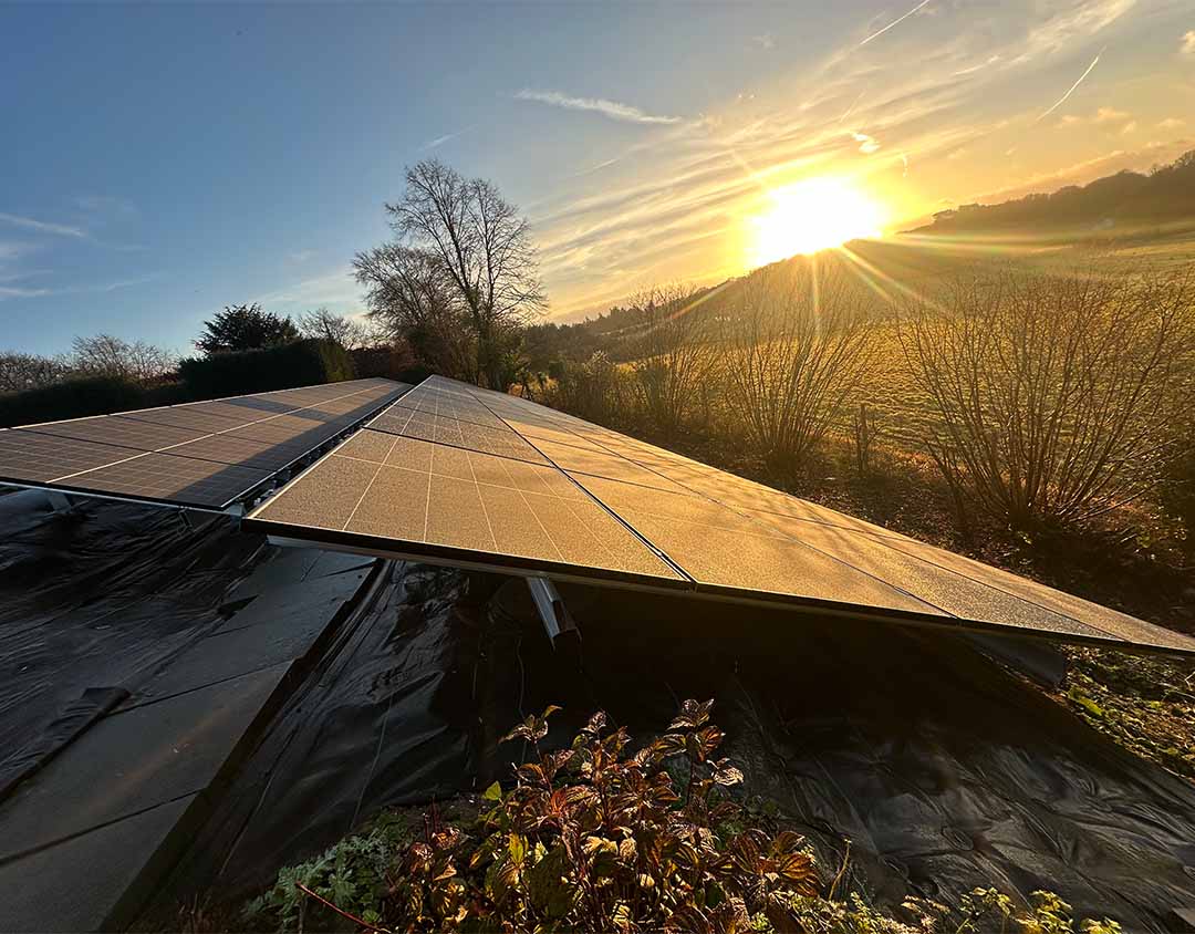 Solar panels on a south-facing slope at sunset, showcasing optimal positioning for maximum energy generation in rural Guildford.