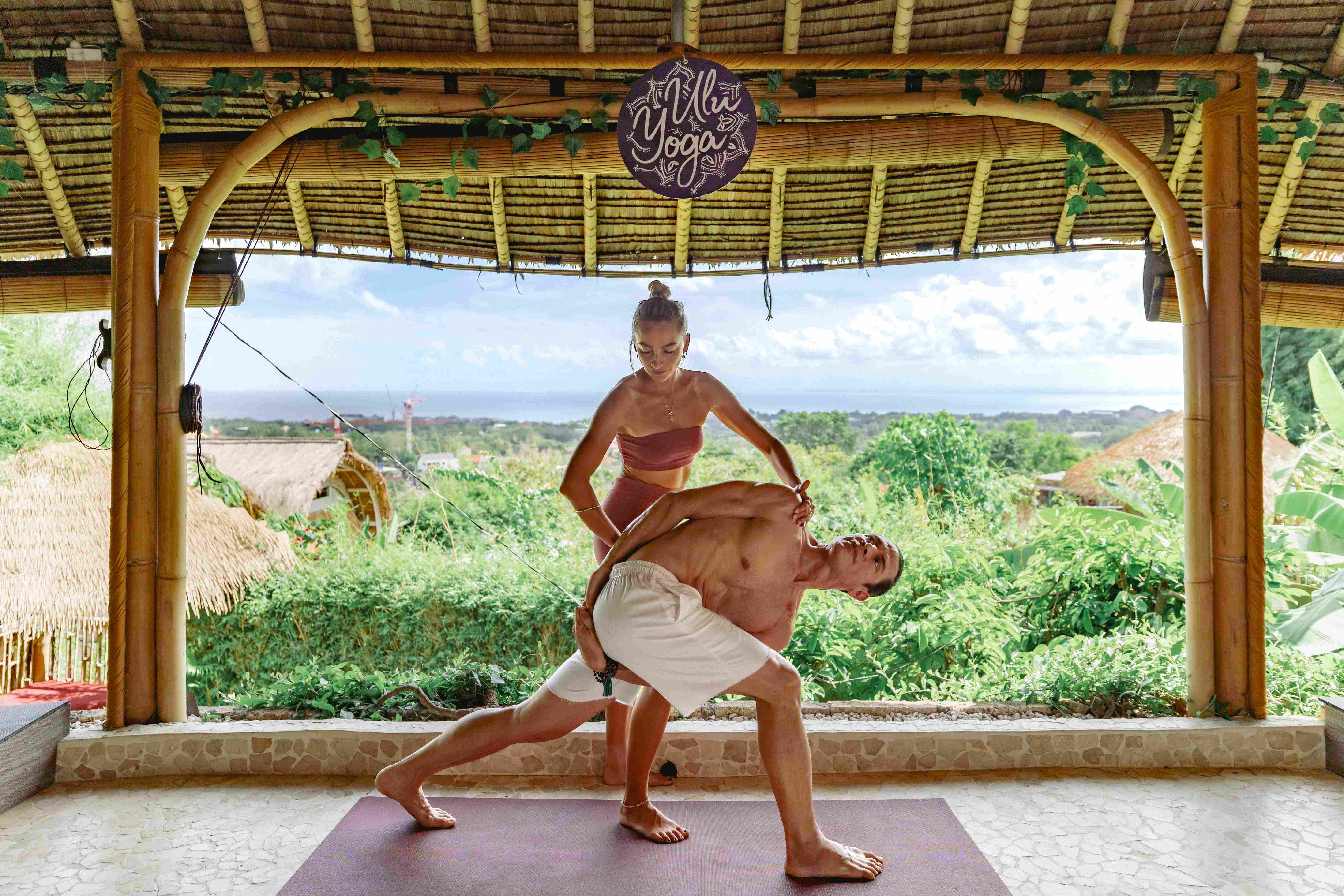 Instructor providing hands-on alignment adjustment to a student during yoga teacher training in the bamboo ocean-view shala.
