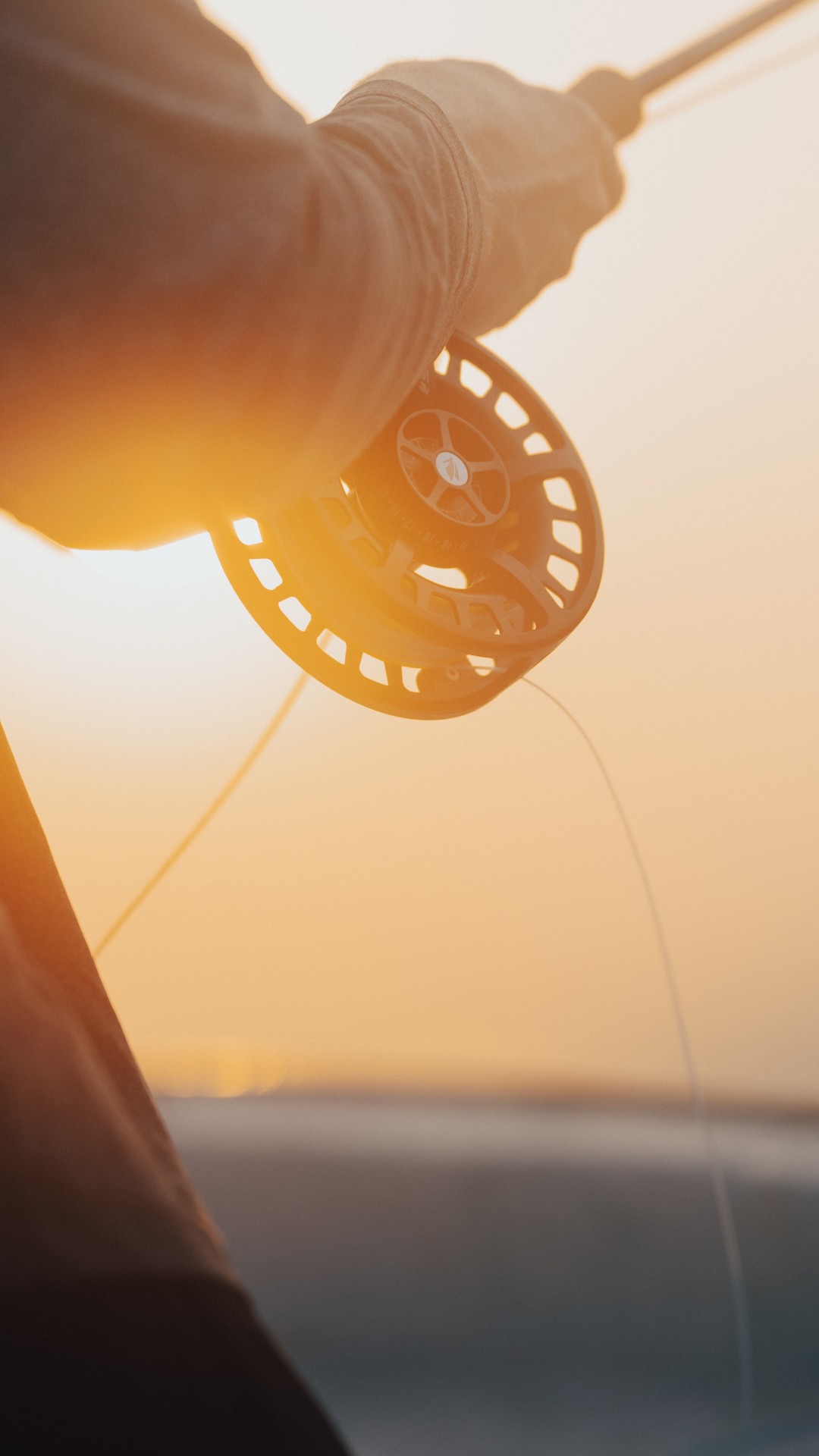 Closeup of a fly reel and an angler holding it during sunset