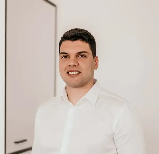 Minimal studio portrait of a confident woman in a white shirt, arms crossed, on a soft gray background.