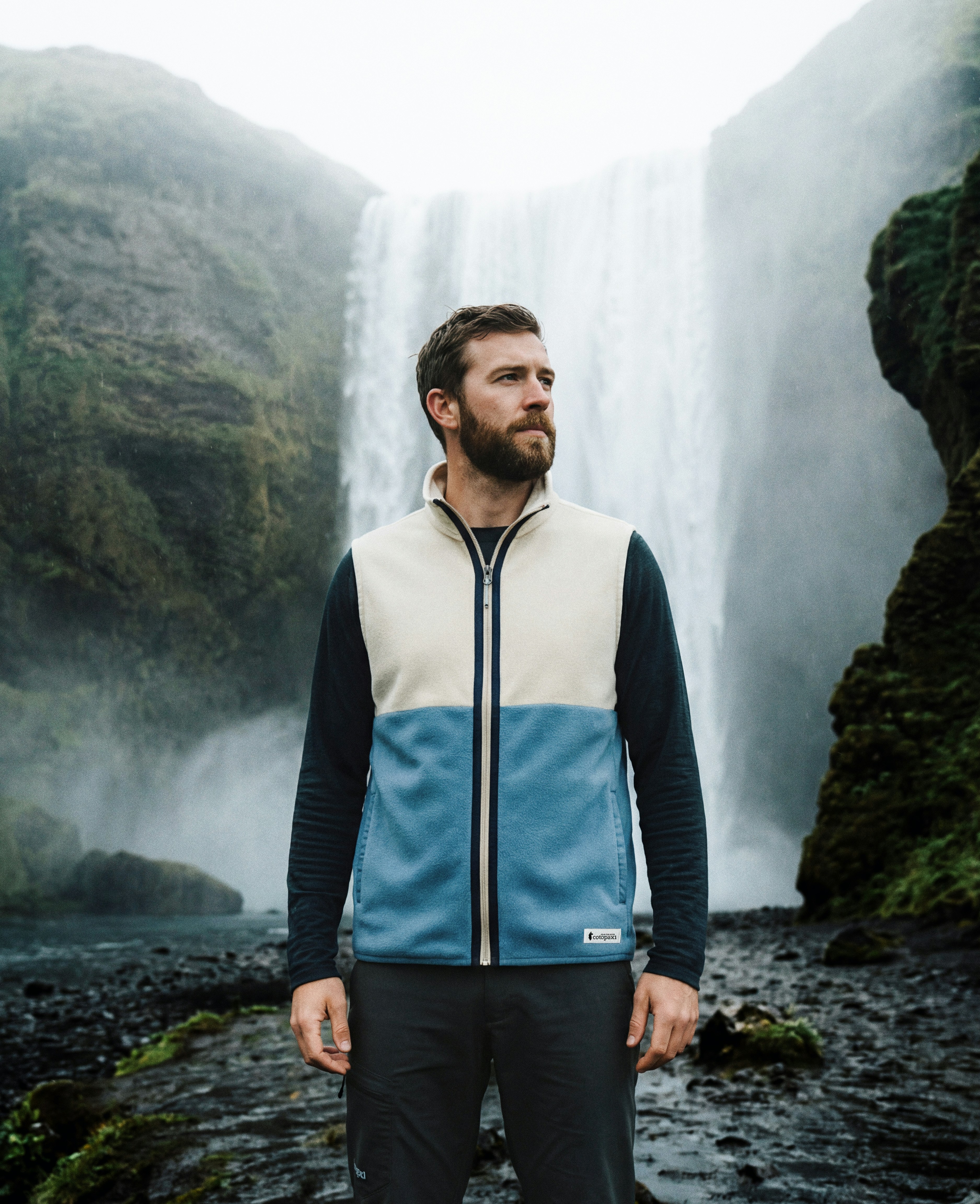 Man in outdoor gear stands before a waterfall
