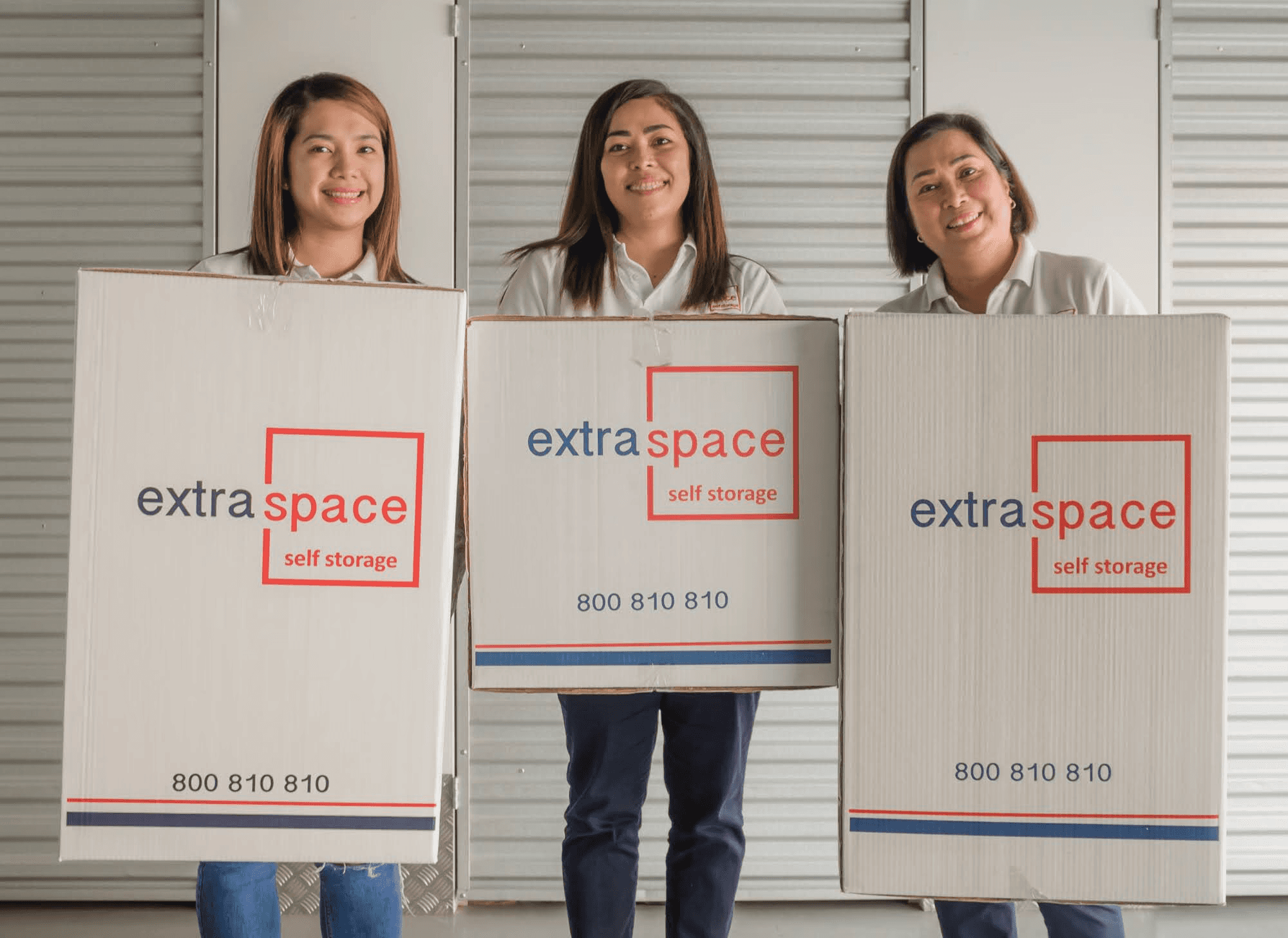 Three professional movers holding Extra Space boxes in a storage facility for an easier move home.