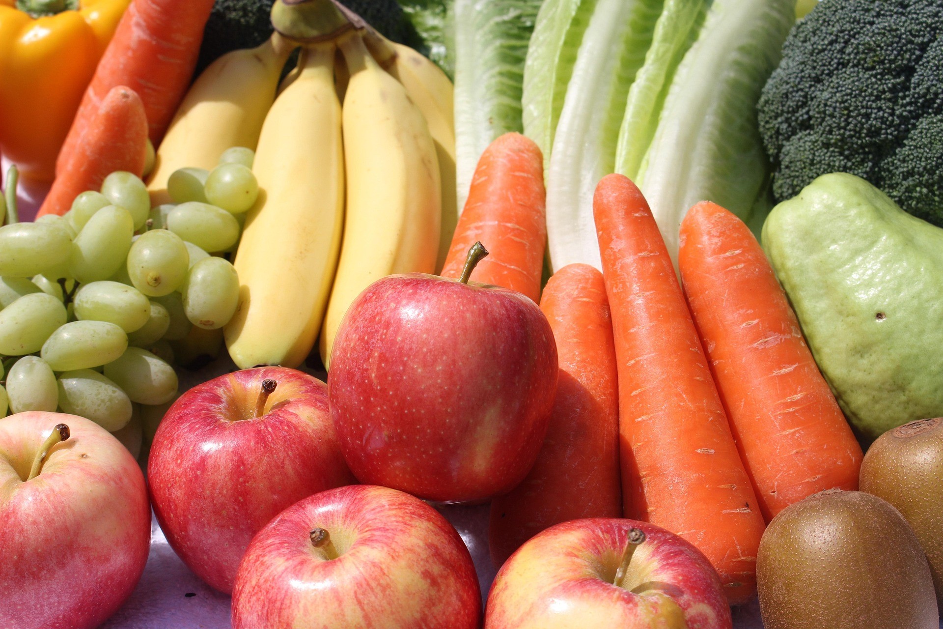 A close-up of fruits and vegetables, including apples, bananas, grapes, carrots, lettuce, and broccoli.