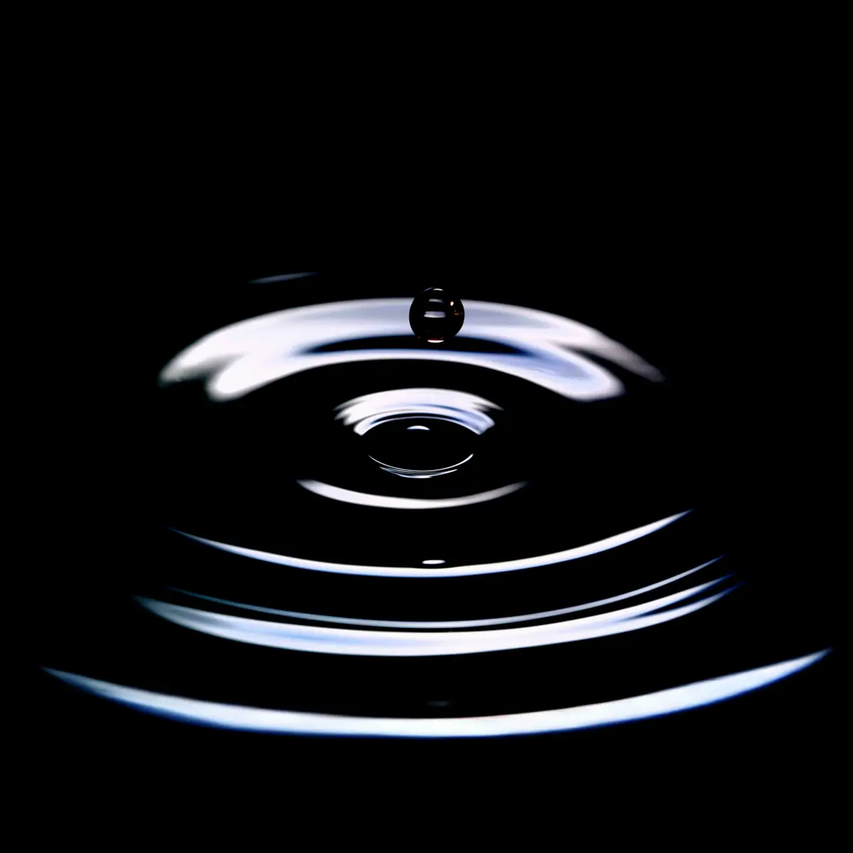 A water droplet captured at the moment it hits a dark surface.