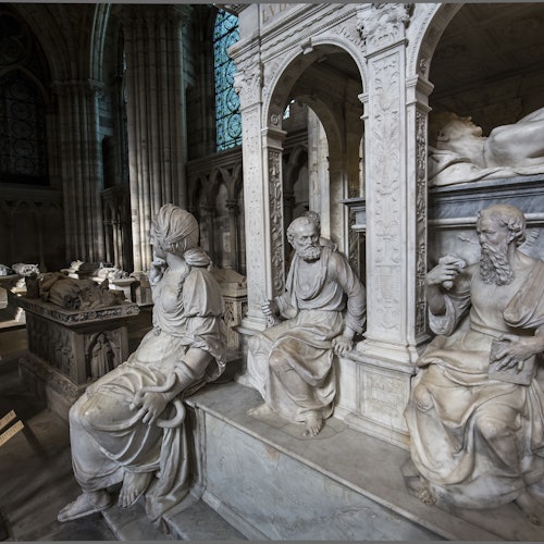在一个历史悠久的大教堂里，有大理石雕刻的坐着的人物雕像，背景是错综复杂的细节和拱形结构。