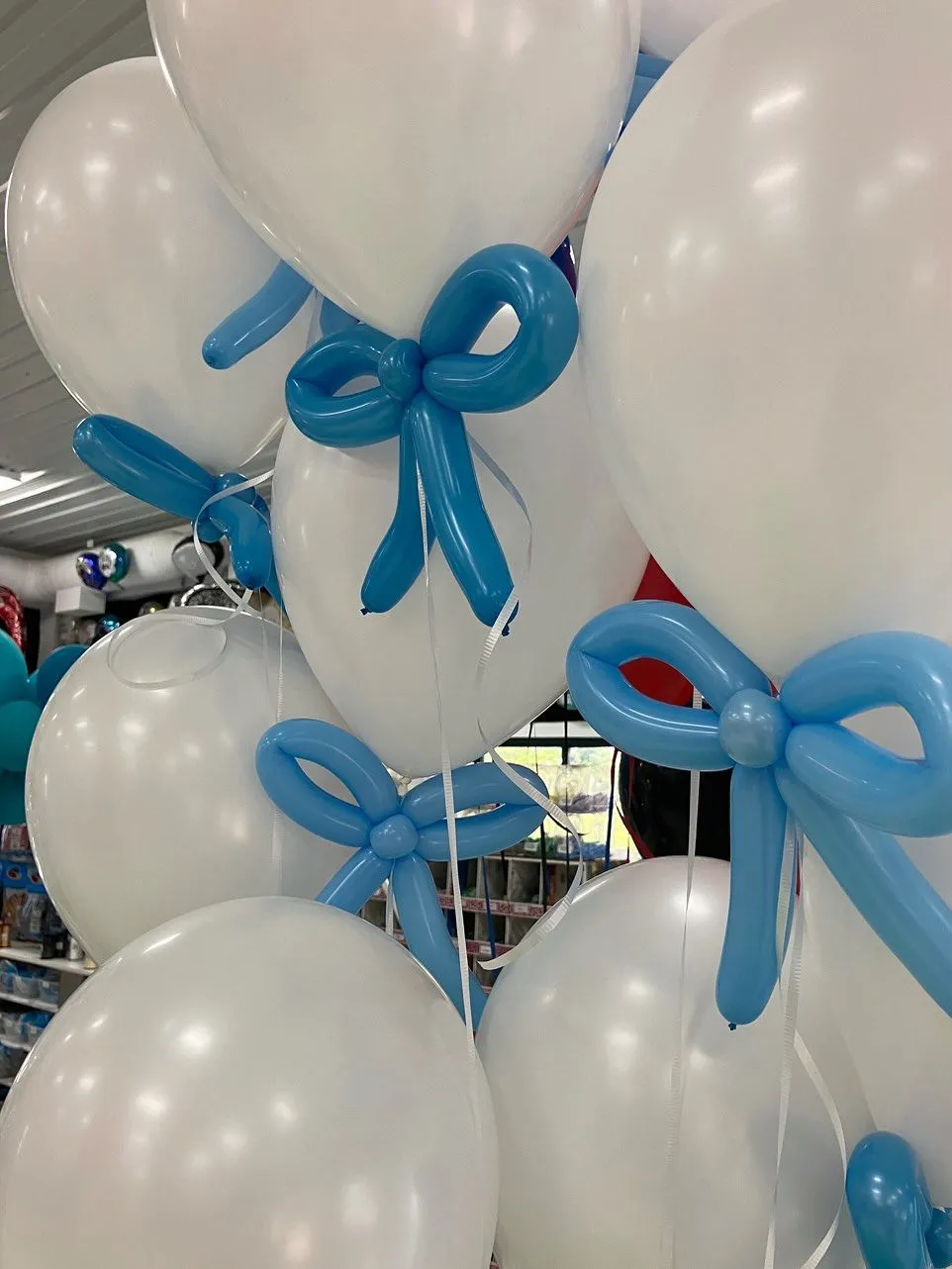 A cluster of white balloons with elegant blue balloon bows is displayed in a well-lit room, creating a festive and cheerful atmosphere.