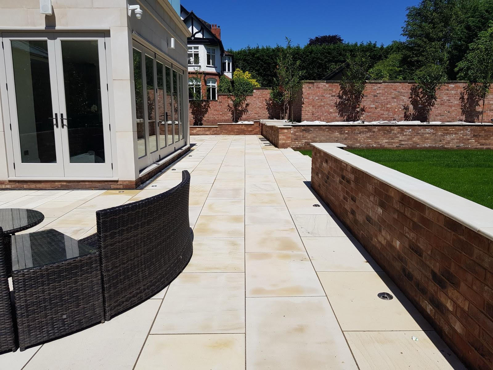 Luxury Wilmslow, Cheshire Garden Transformation by LK Landscaping and Groundworks - Large-format limestone patio tiles, custom brick retaining walls, and stylish rattan furniture create an elegant outdoor living space. Expert hardscaping and landscaping services for high-end residential properties.