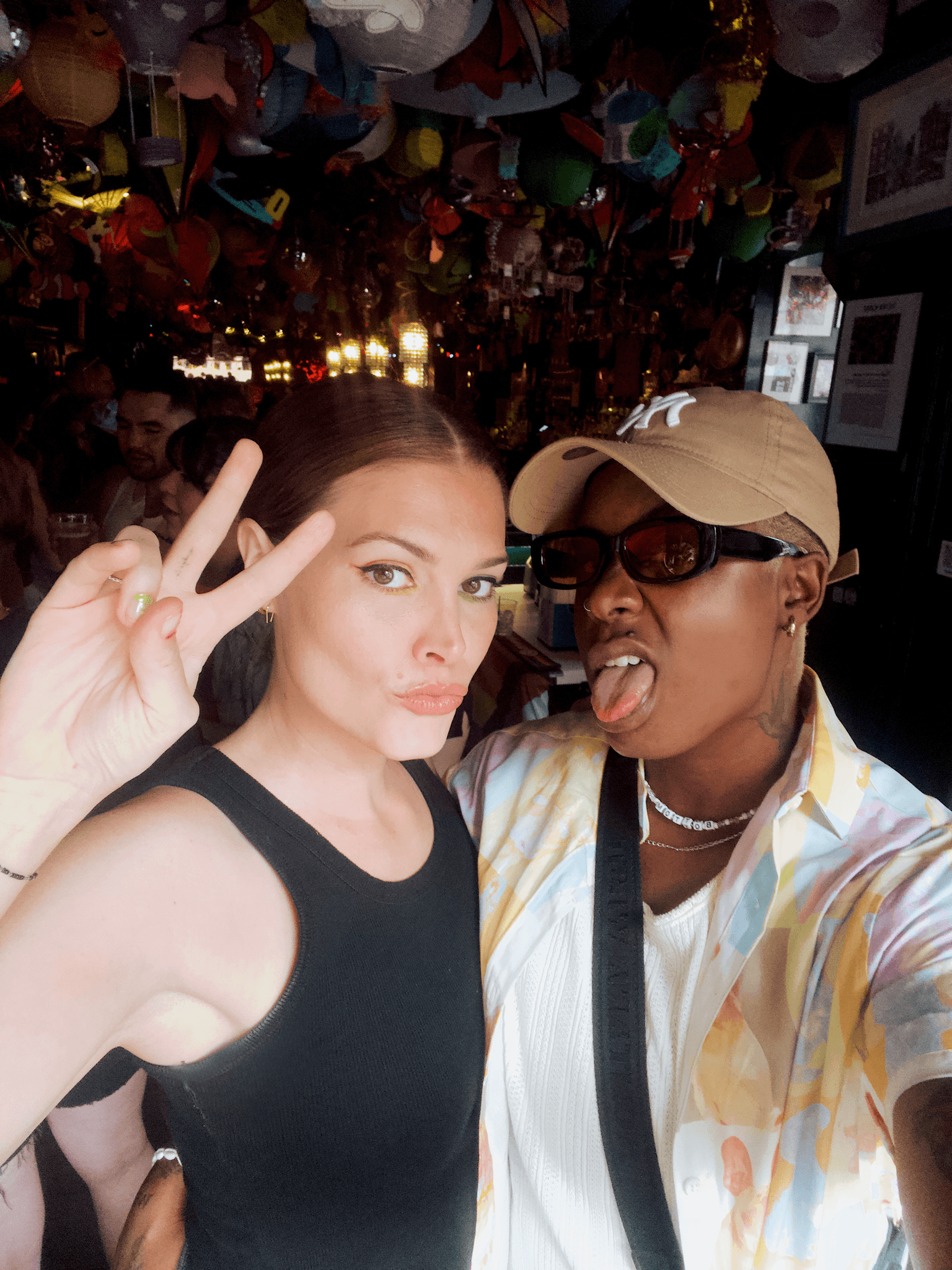 A selfie of Ashleigh Warren and her partner, Jessica Smith smiling. One is making a peace sign, with colorful decorations in the background.