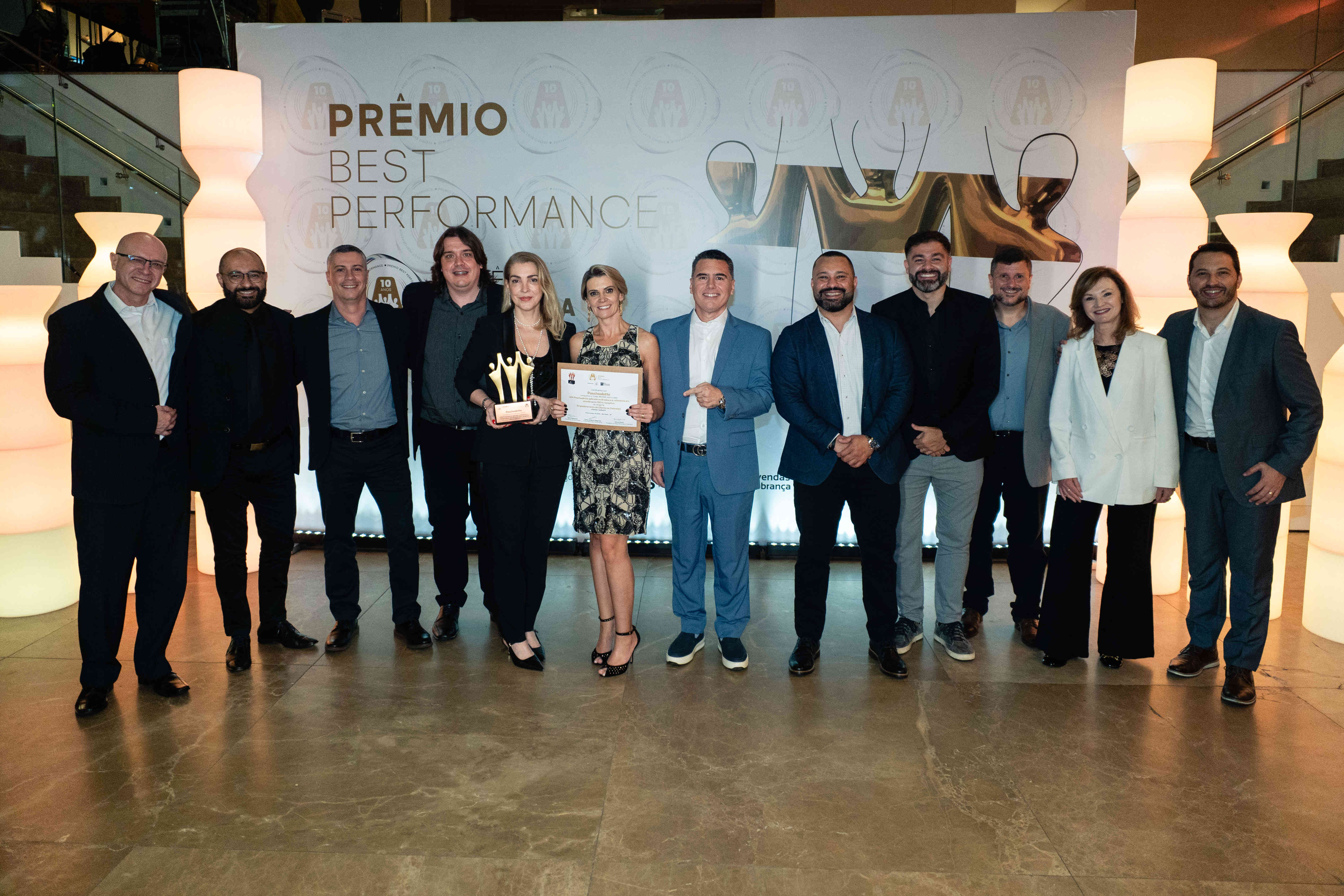 Executivos da Paschoalotto posando com troféu bronze e certificado no palco do Prêmio Best Performance 2025