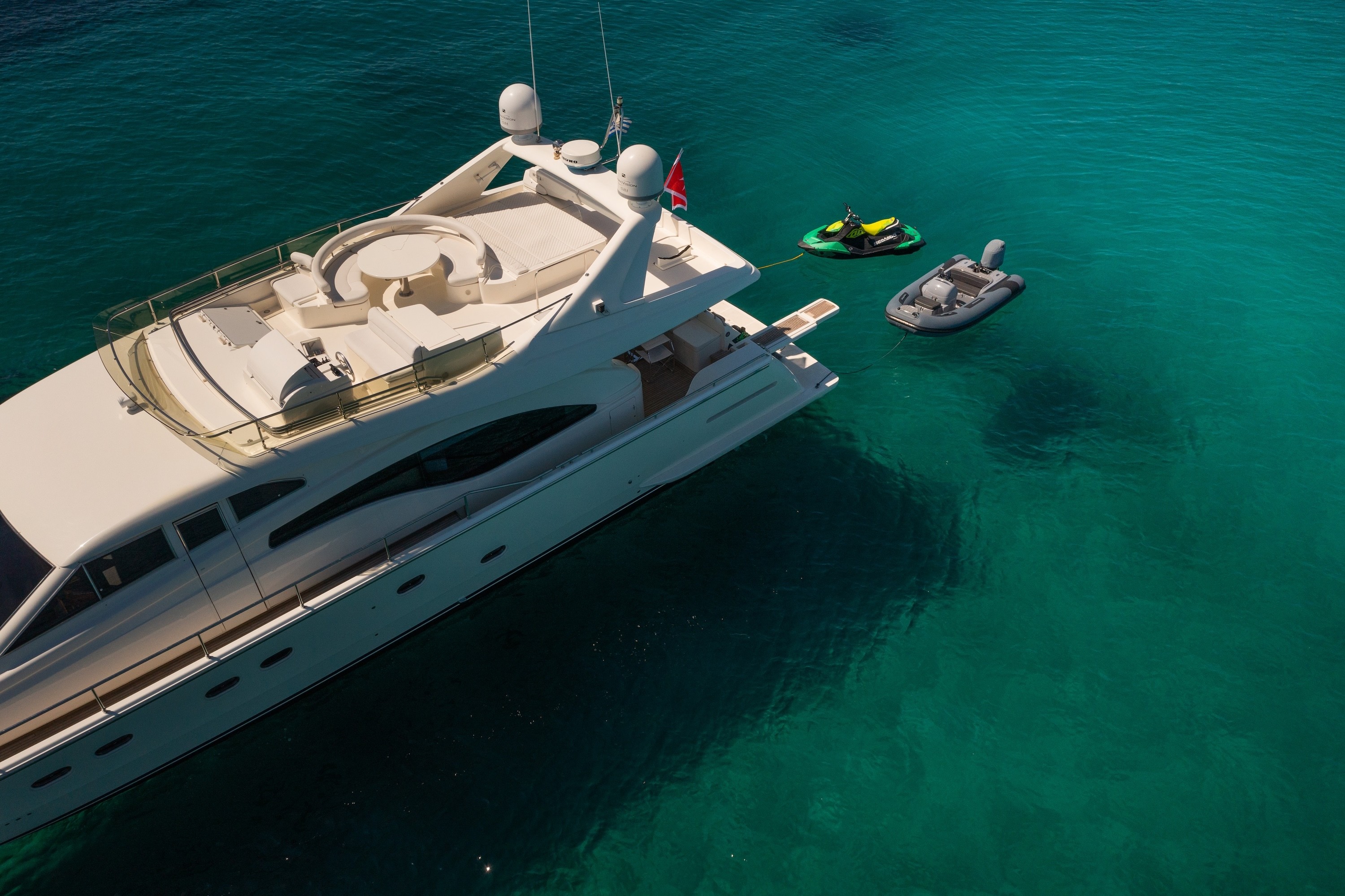 Aerial view of luxury motor yacht Ferretti 68 Simply Brilliant anchored in turquoise waters with water toys nearby.