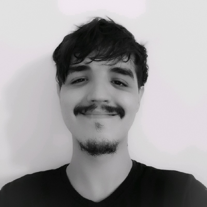 A person with wavy hair and a goatee smiles warmly at the camera, wearing a casual dark t-shirt against a simple, light background.