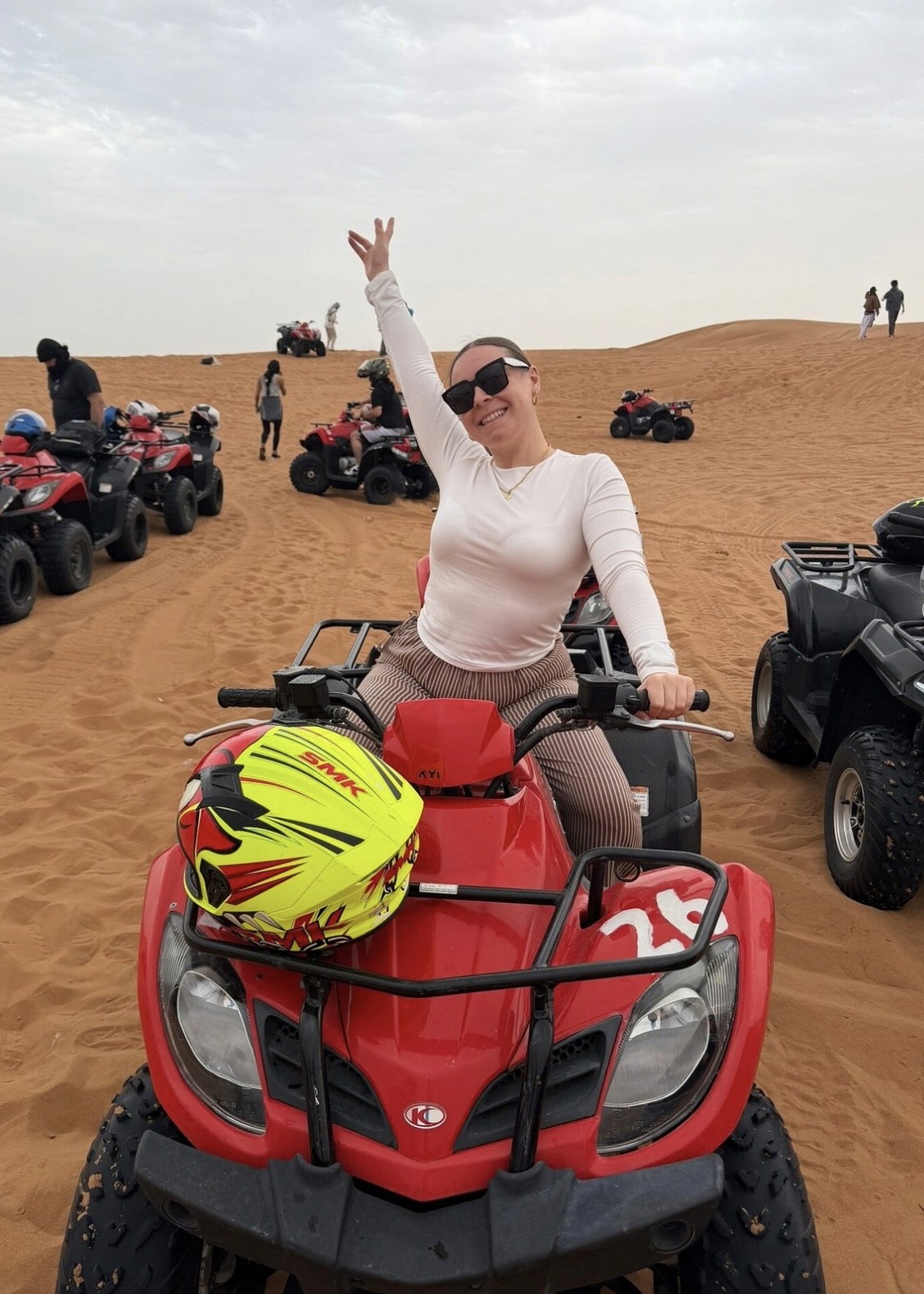 A female traveler smiling and cheering on a red quad bike during a desert safari excursion in Dubai