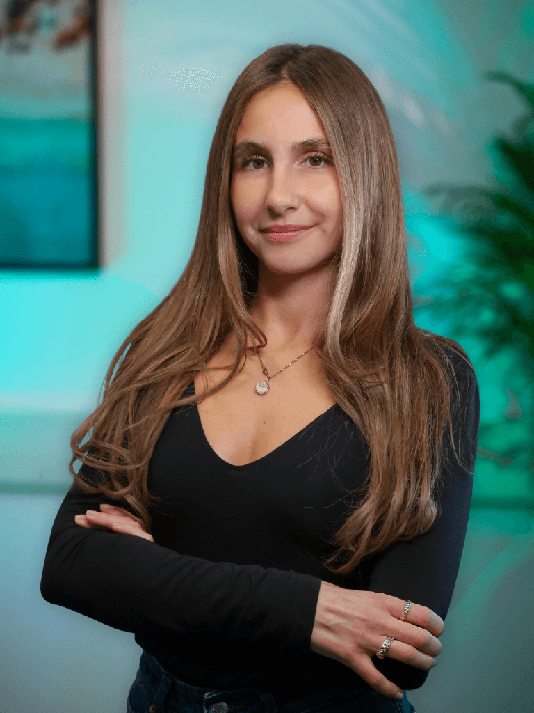 A woman with short curly hair wearing a black t-shirt looks into the camera.