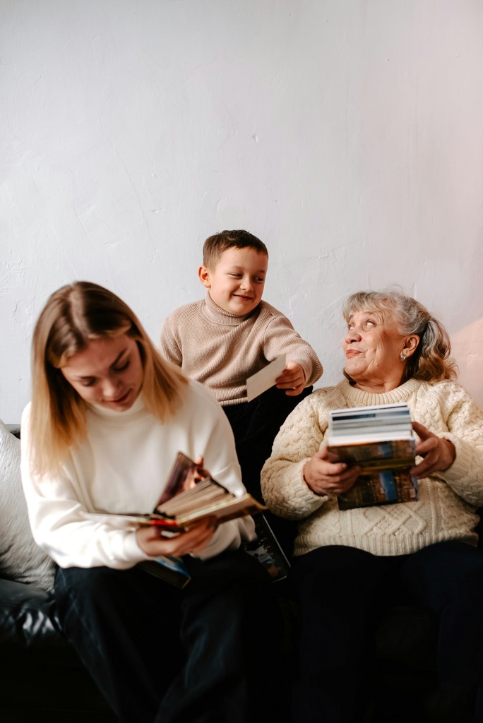 A young boy, a teenager, and an elderly woman share a joyful moment while looking through a collection of photographs and albums, highlighting the importance of family memories and intergenerational bonds.