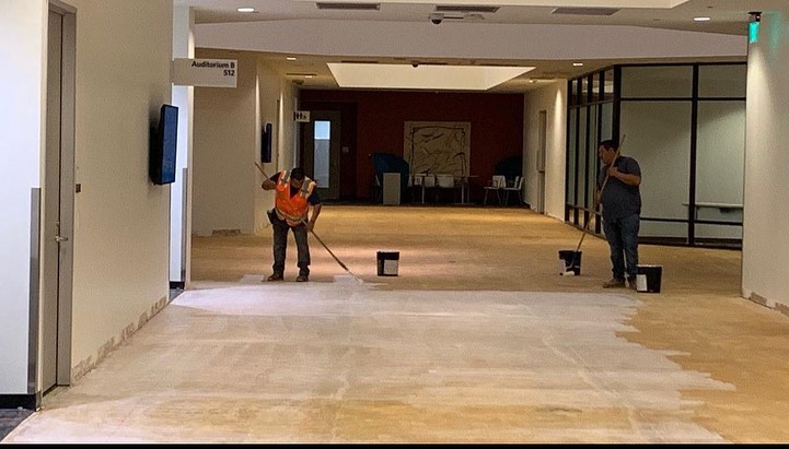 Bare subfloor in an office corridor being swept before carpet tile goes down