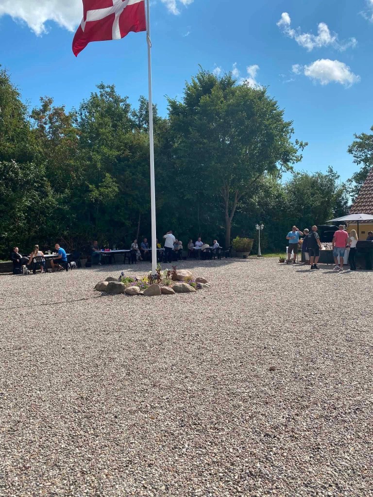 Dannebrog på gårdspladsen, borde i skyggen og grill under parasol