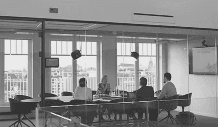 Three people in conversation with warm lighting, including a person wearing a hat and another person wrapped in what appears to be a textured shawl or sweater.