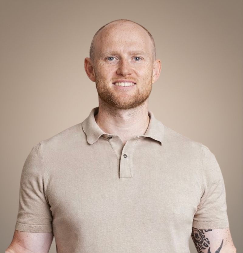 A confident person with short, styled hair and a leather jacket poses against a dark backdrop.