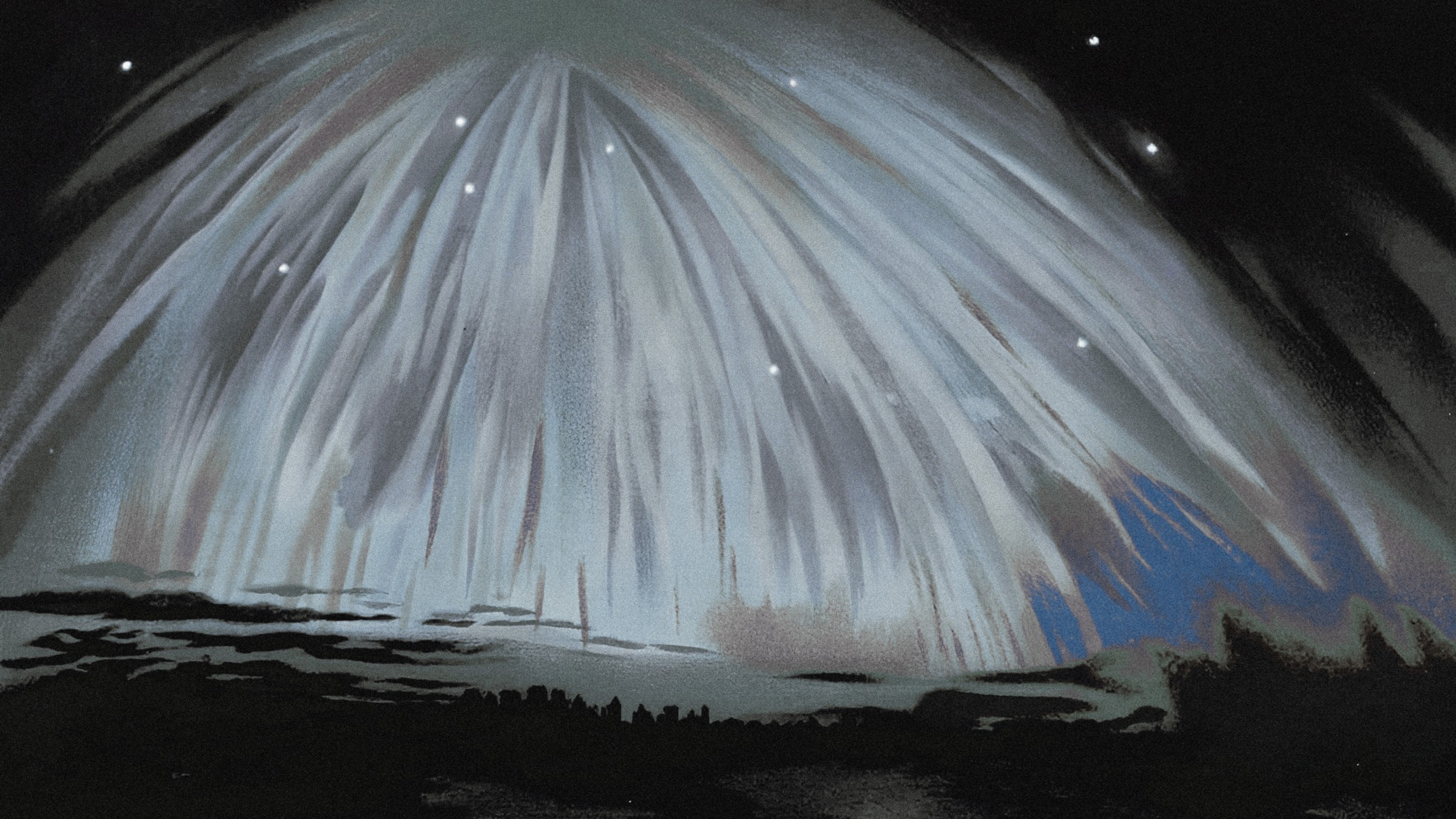 A wide, hazy landscape under a pale blue sky with scattered white clouds, featuring rolling, sandy hills in the distance and dry, yellow grass and green bushes in the foreground.