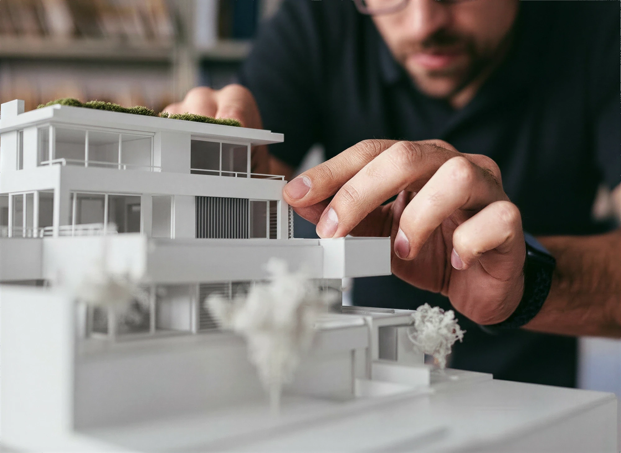 Architect adjusting white massing model of modern house on desk.