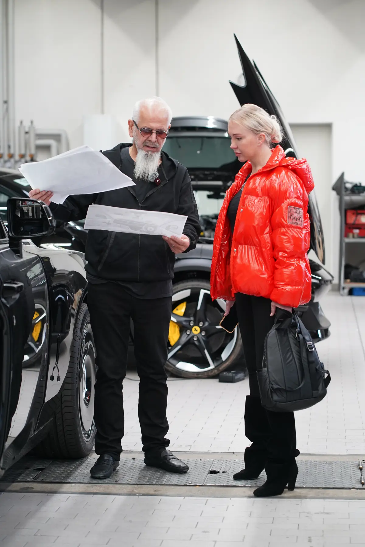 Elena and Kourosh Mansory reviewing design plans inside the Mansory factory with a Ferrari wheel visible in the background