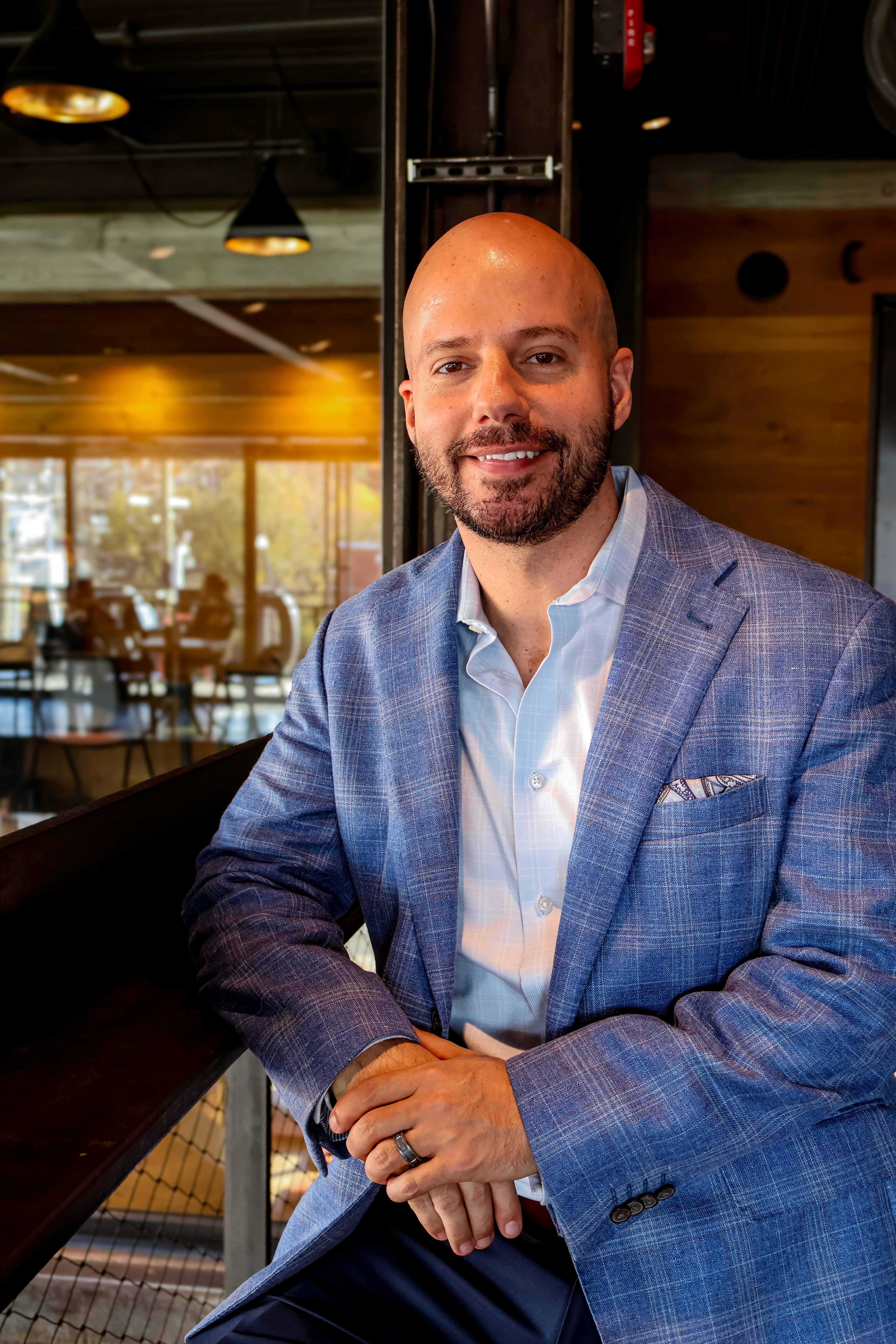 Portrait of a young man in a brown coat and beige turtleneck, with light brown hair and a calm expression against a gray background.