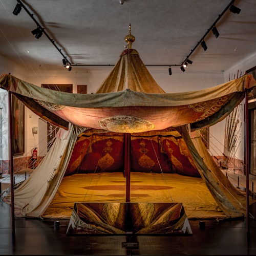 一个装饰华丽的历史帐篷陈列在灯光柔和的博物馆房间中。