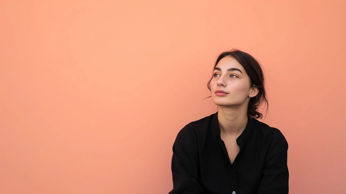 Young woman in black shirt against peach background, looking contemplative. Simple, elegant portrait with soft colors.