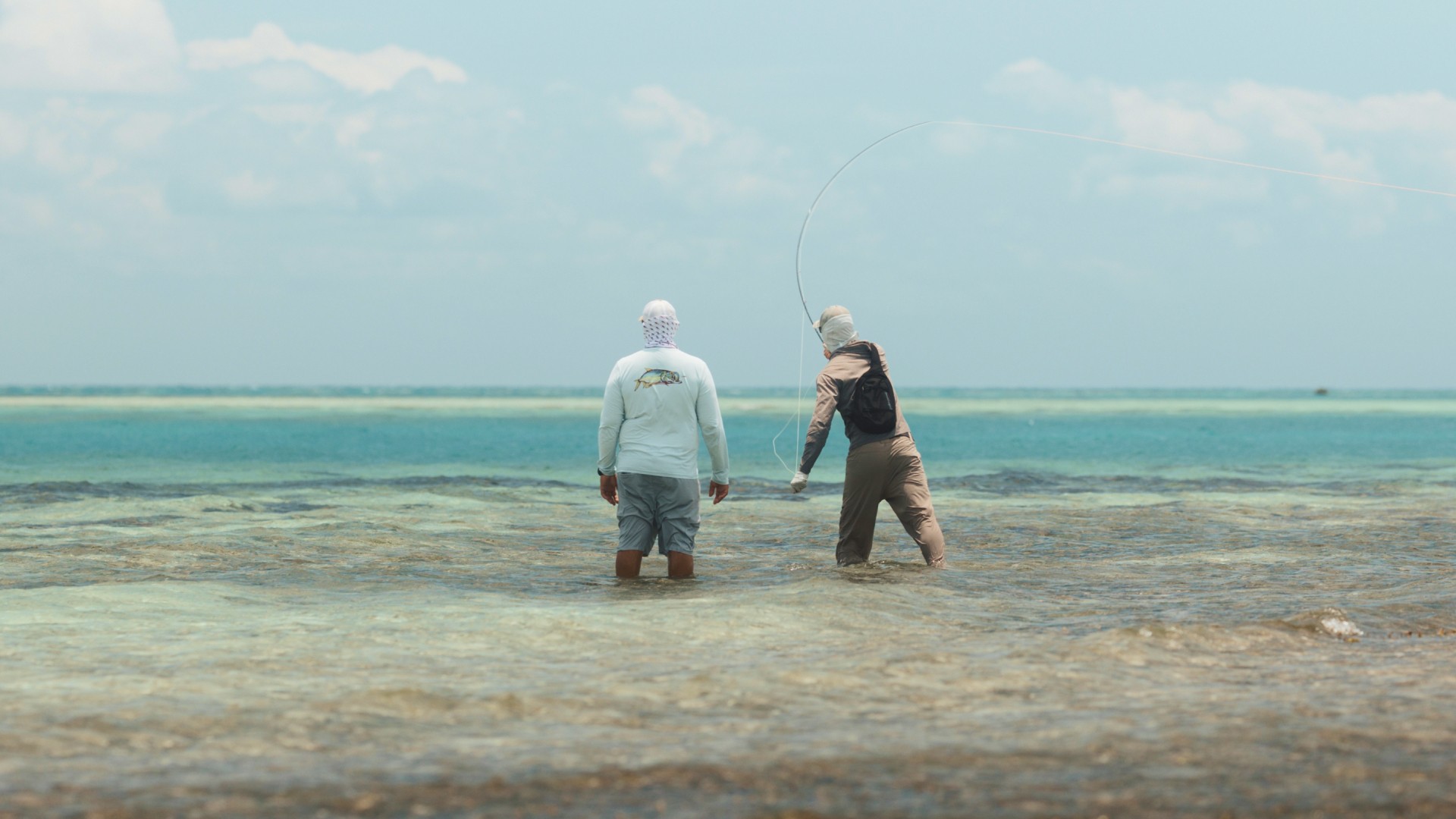 Saltwater angler casting a fly rod with a fly fishing guide by his side
