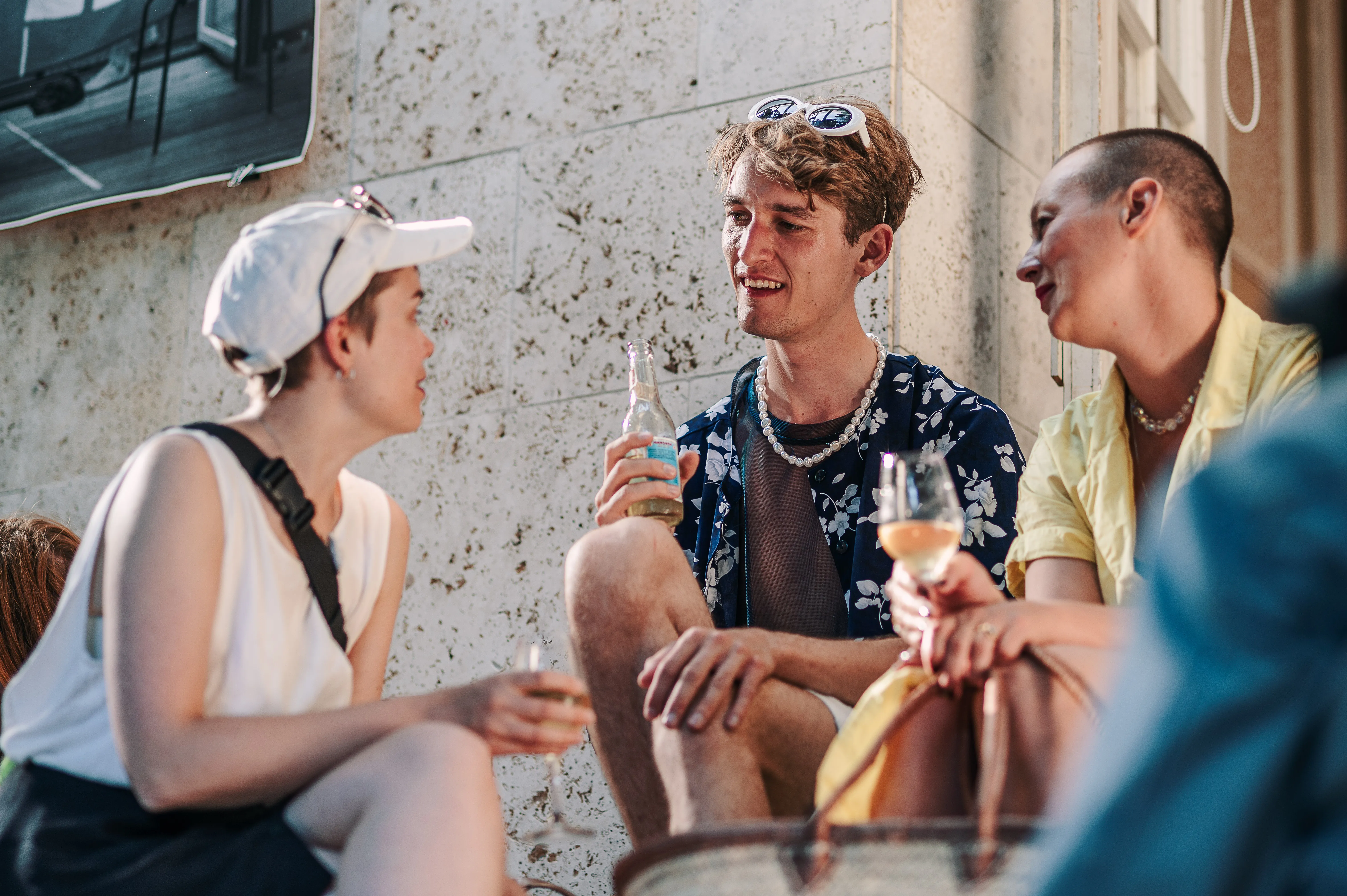Unge kulturgængere drikker champagne mens de sidder på kantsten.