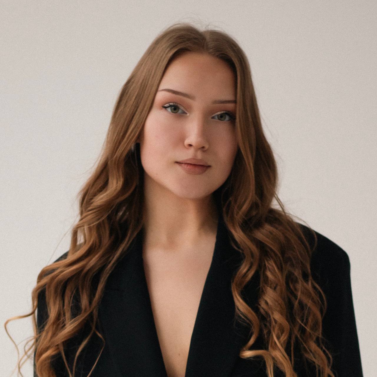 Portrait of Lizaveta Hancharenka - Co-Founder & CPO, young woman with long wavy brown hair, wearing a black blazer. She is looking directly at the camera.