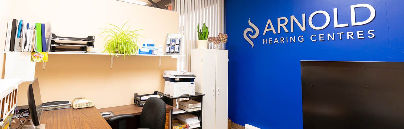 A modern workspace featuring a wooden desk and a blue wall with the text "ARNOLD HEARING CENTRES" prominently displayed.