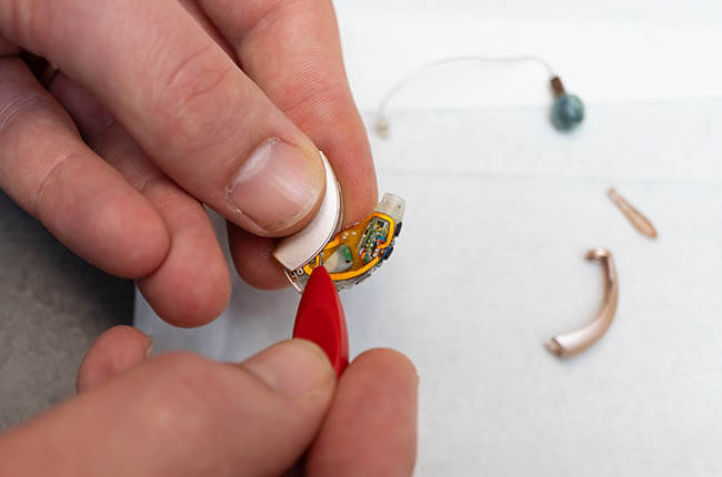 A close-up of a hand assembling small components, including a circular piece and a red tool, on a flat surface.