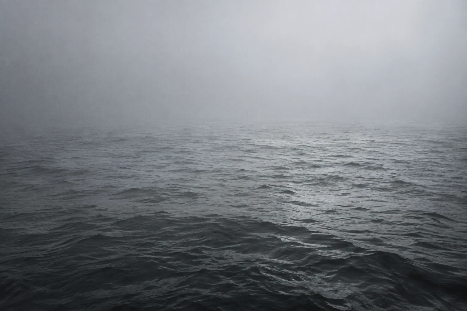 Dark silvery sea disappearing into dense gray fog, no coastline, subdued monochrome