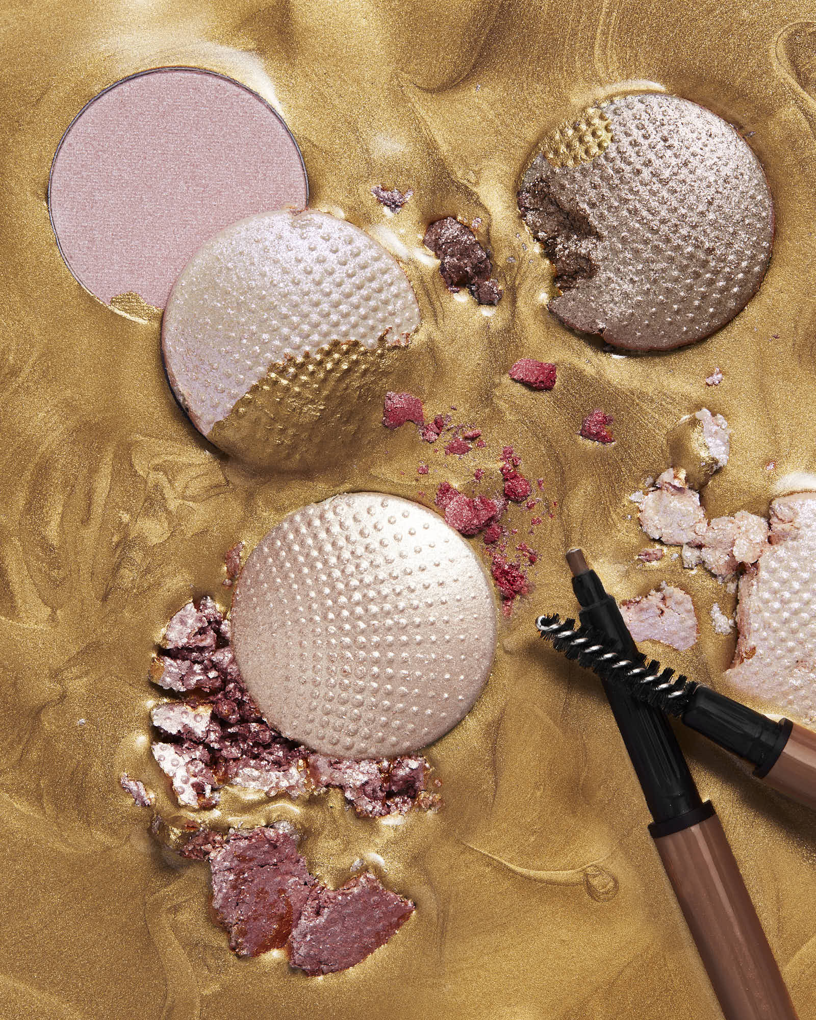 Shimmering makeup palette with brushes on gold background.