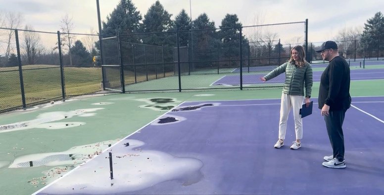Athletic director inspecting puddling and surface damage on aging school tennis court for long-term budget planning