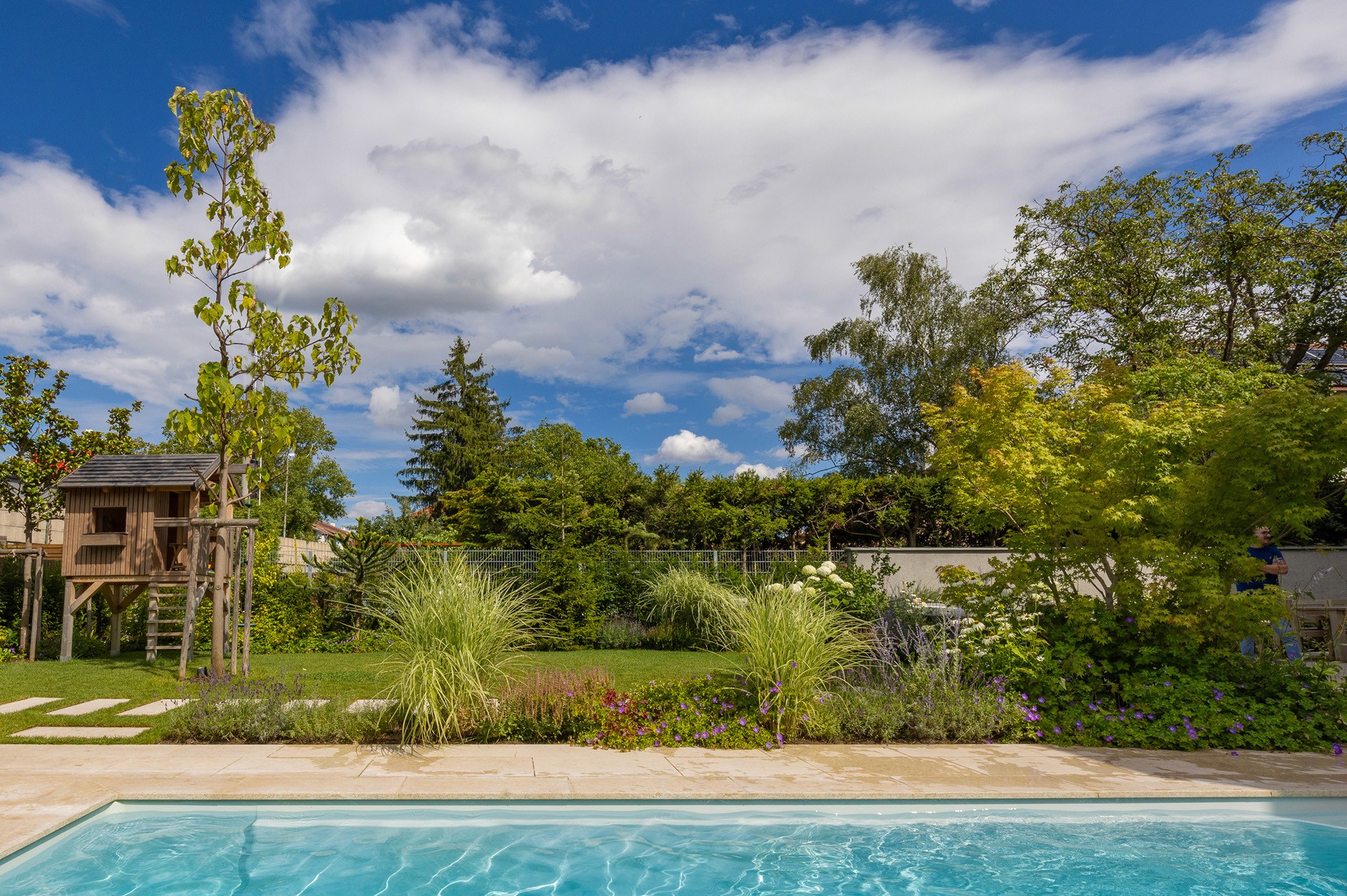 Garten mit Pool, Rasen und Holzbaumhaus.