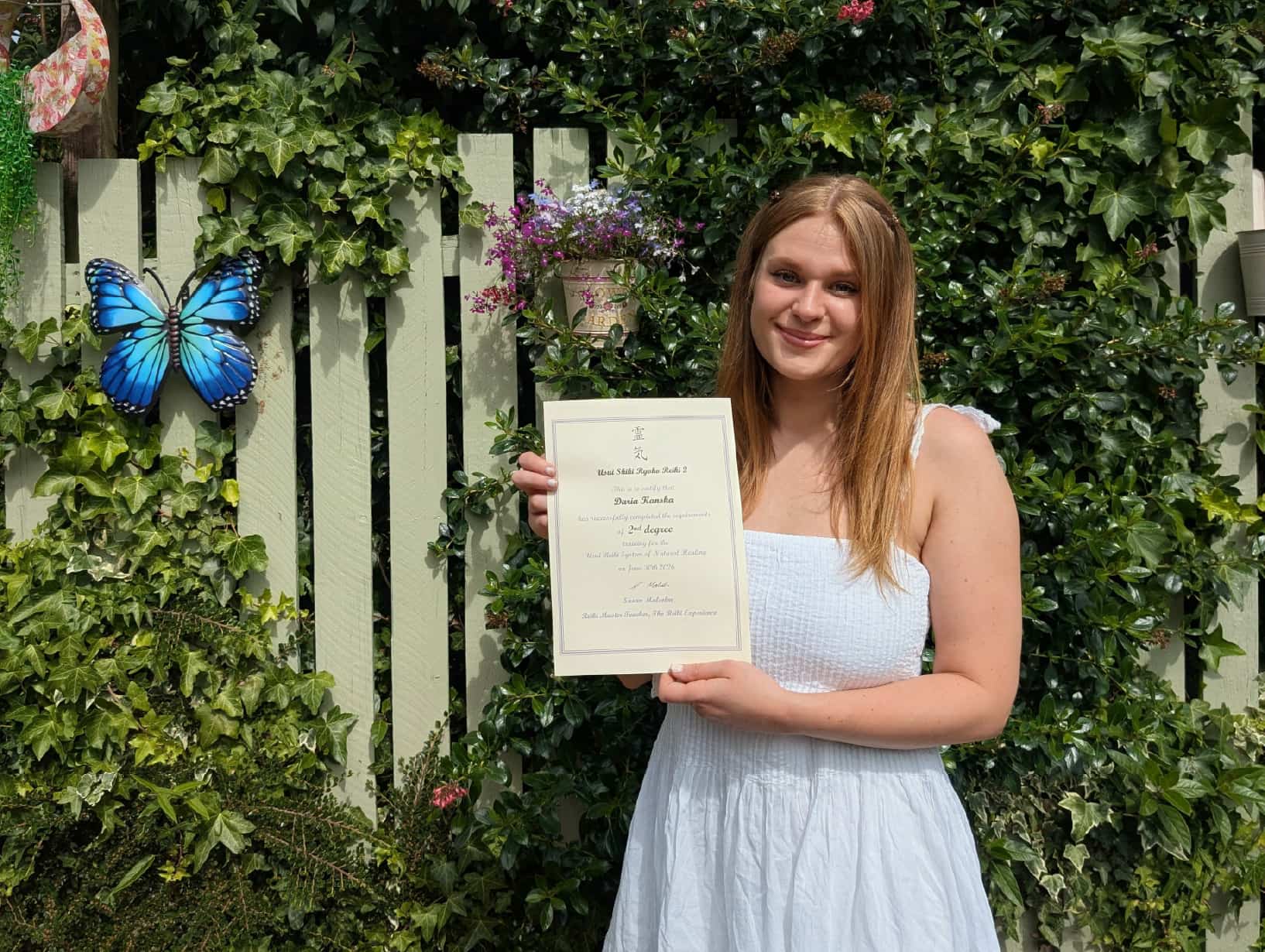 Daria holding her Usui Reiki Level 2 Practitioner certificate outdoors.